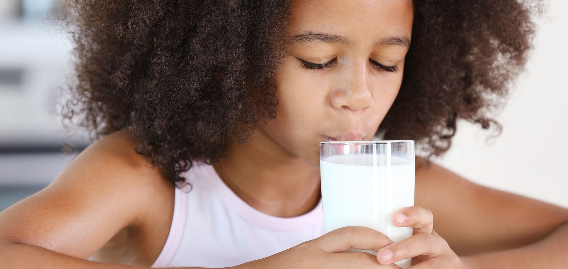 Little girl drinking a glass of milk at the kitchen table
