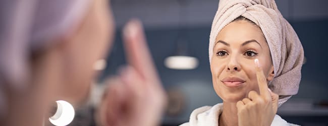 Woman applying face cream in front of a mirror